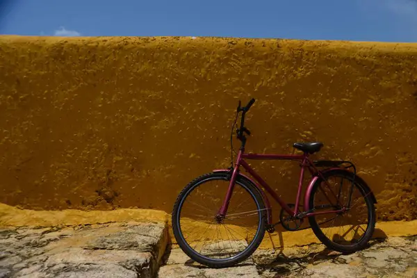一辆红色自行车靠在蓝色天空下的黄色墙壁上 — 图库照片