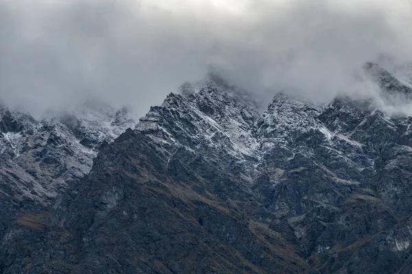 ニュージーランドのクイーンズタウンで霧の多い日に雪に覆われた岩場の山の峰 — ストック写真