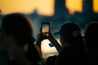 Deniz kenarında gün batımının fotoğrafını çeken güzel bir kız resmi. Telefonla.
