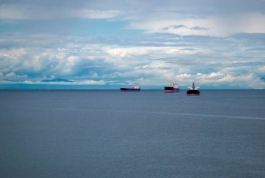 Kabarık beyaz bulut arka planında ufukta seyreden üç geminin yakın görüntüsü.