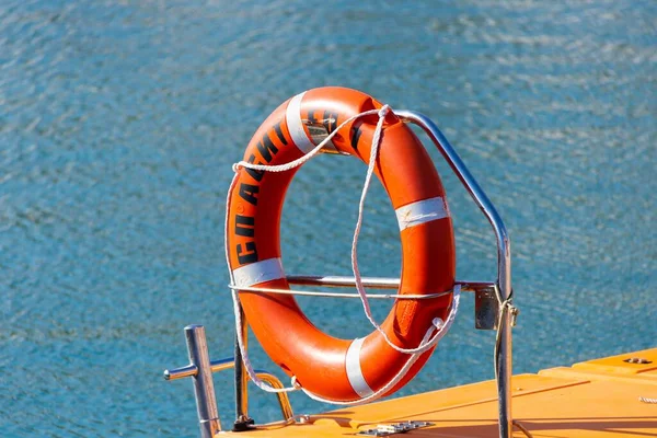 A red life buoy on a boat with a blue ocean in the background in sunny weather