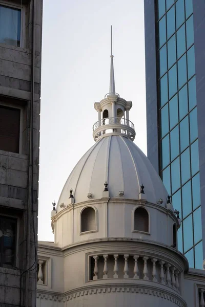 背景には近代的な建物や高層ビルが立ち並ぶ白い教会のドームの垂直ショット — ストック写真