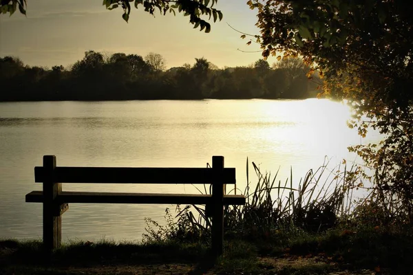 stock image A scenic view of the reflection of bright sun in the lake with wooden bench on the shore