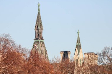 Ağaçların arkasındaki iki kilise kulesi açık mavi gökyüzüne karşı.