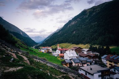 Orman dağları ve bulutlu arka planla çevrili yüksek bir şehir manzarası.