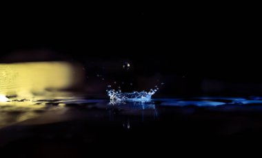 Siyah arka planda suya düşen bir damlacığın yakın plan görüntüsü.