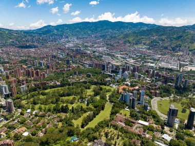 Güneşli bir günde yüksek binalar ve yeşil doğa ile Medellin şehrinin havadan görünüşü.