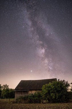 Samanyolu ve yıldızlı gökyüzünün küçük bir kırsal ev üzerindeki dikey görüntüsü