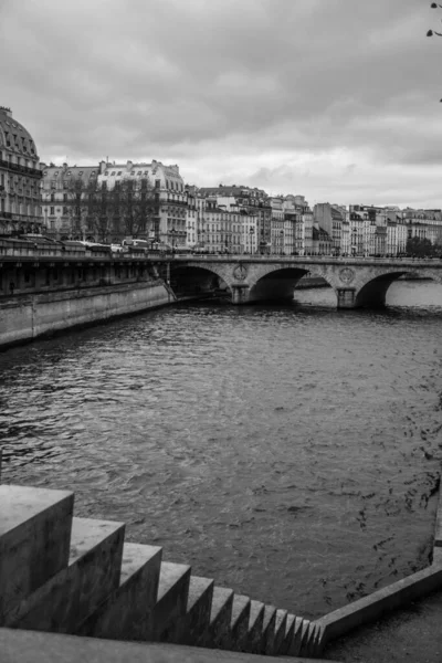 以城镇景观为背景的河流上一座旧桥的垂直灰度 — 图库照片