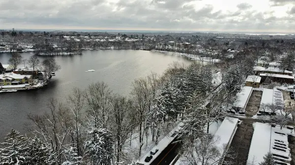 チラシの木や雪に覆われた町の建物に囲まれた湖 — ストック写真