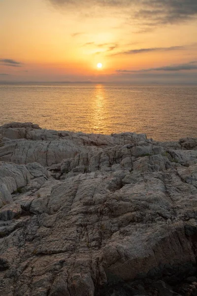 岩場の崖の上の垂直ショットと静かな海の表面を着色夕日 — ストック写真