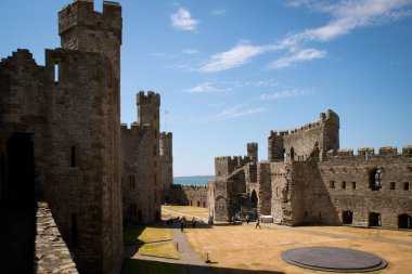 Caernarfon Kalesi 'nin Galler' deki mavi gökyüzüne karşı manzaralı bir çekimi.