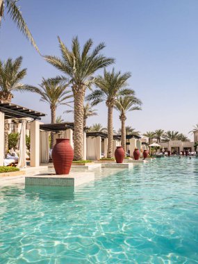 Al Wathba Desert Resort ve Spa 'da palmiye ağaçları ve kabinlerle dolu uçsuz bucaksız sonsuz bir havuz.