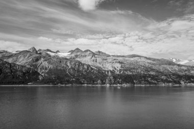 Arka planda bulutlu bir gökyüzünün altında karlı dağlar olan sakin bir denizin gri pulu.