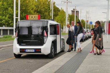 Beyaz bir ETIOCA tam elektrikli minivan taksisine binen insanların görüntüsü.
