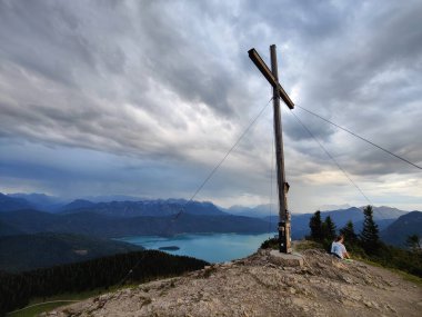 Bulutların altında bir tepenin üstünde haçla güzel bir deniz manzarası.