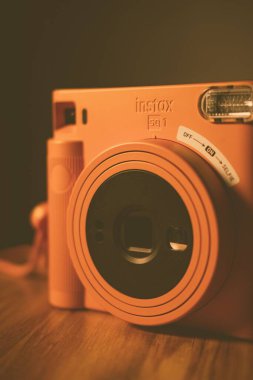 Ahşap bir masanın üzerindeki Fuji Instax Meydanı 'nın yakın çekim görüntüsü loş ışığın altında.