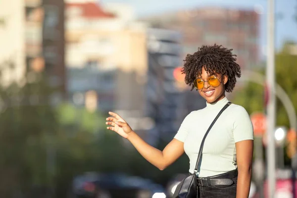 stock image A beautiful afro-haired young woman standing on the street and taking a taxi with her hand up