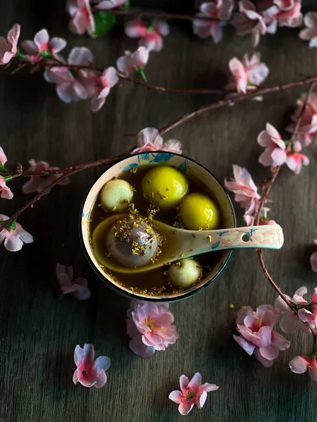 stock image A vertical closeup of a bowl of Tangyuan on a table decorated with pink flowers.