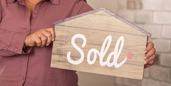 stock image A woman holding house-shaped paper with the word sold printed on it