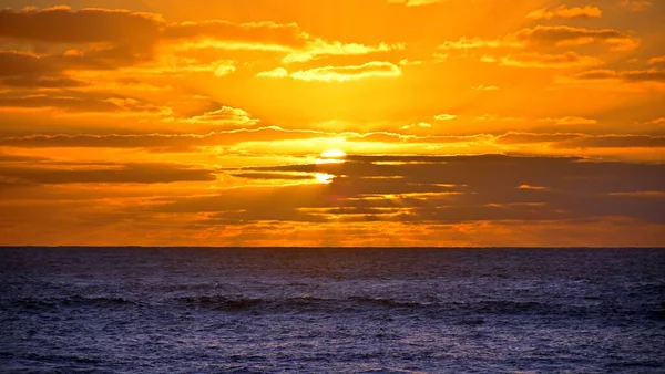 波打つ海の上に抽象的な雲と美しい黄色のオレンジ色の夕日の空の絵のような景色 — ストック写真