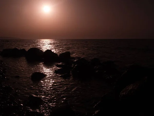 stock image A seascape view with light reflecting on water stones around, cloudy sky and sun background