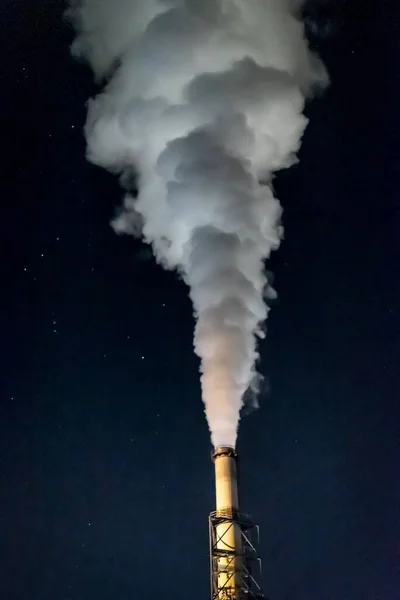 총거리는 밤하늘의 배경에서 연기를 방출하는 굴뚝을 수직으로 클로즈업하는 — 스톡 사진