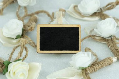 Düğün yaka çiçekleriyle çevrili küçük boş bir karatahta.