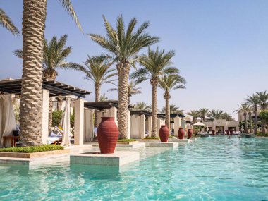 Al Wathba Desert Resort ve Spa 'da palmiye ağaçları ve kabinlerle dolu uçsuz bucaksız sonsuz bir havuz.