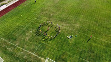 Futbol sahasında çember oluşturan çocukların hava görüntüsü.