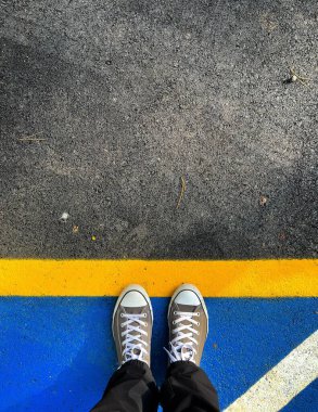 Mavi ve sarı asfalt üzerinde spor ayakkabı giyen birinin dikey görüntüsü.