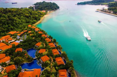 Turkuaz sudaki teknelerin ve Sentosa Adası 'ndaki kırmızı çatıların havadan görünüşü. Singapur.