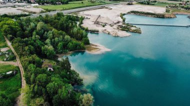 Göl ve ağaçlarla çevrili bir manzaranın havadan görüntüsü.