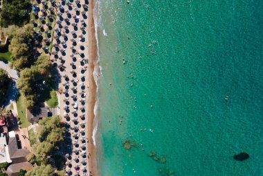 Turkuaz deniz manzaralı Aziz Niklas plajında plaj şemsiyeleri altında tatil yapan insanların antresi.