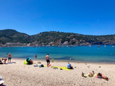 Cala Formentor plajında güneşli bir gün ve insanlar tatilde vakit geçirip güneşleniyor.