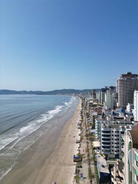 Açık mavi gökyüzünün altında kıyı şeridine bakan binaların dikey görüntüsü.