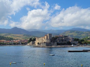 Mavi bulutlu gökyüzünün altında arka planda dağ olan antik bir deniz şatosu.