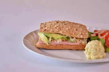 Yanında salata ve çırpılmış yumurta ile servis edilen jambonlu ve avokadolu bir sandviç.