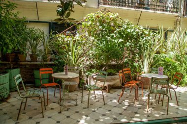 Eski model mobilyalı bir kafe, açık havada, saksıda bitkiler, arka planda tuğla duvarlar, güneşli bir günde.