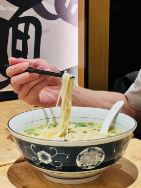 Yemek çubuklarıyla erişte tutan bir elin dikey görüntüsü.