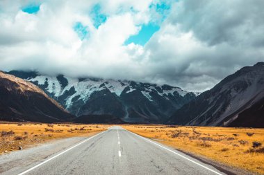 Mavi gökyüzünün altındaki dağlık bir araziye uzanan asfalt bir yol.