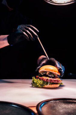 Şefin dikey resmi siyah eldivenli elleri sulu hamburgerin içine sığır pirzolası koyuyor.