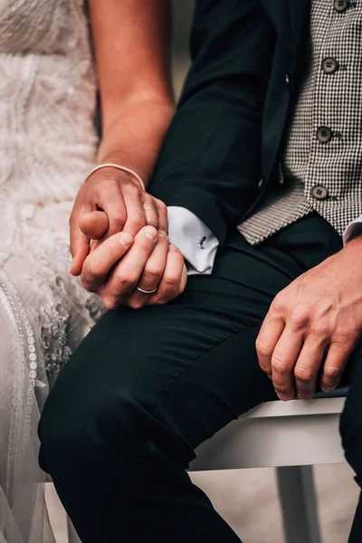 ベンチに座って手を取り合っている新婚夫婦の垂直ショット — ストック写真