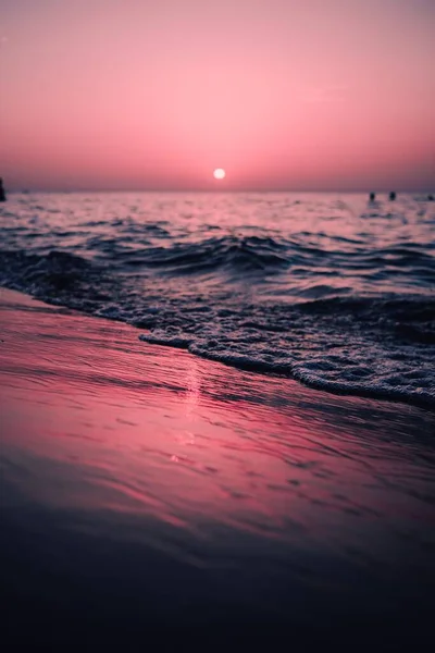 背景には雄大な赤い太陽が輝くビーチで展開する海の波の垂直ビュー — ストック写真