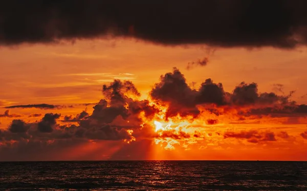 オレンジ色の空を背景に海に沈む夕日 雲の中から差し込む光 — ストック写真