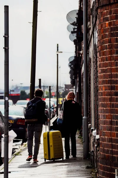 明るい黄色のスーツケースを持つ通りの歩道を歩くカップルの垂直ショット — ストック写真