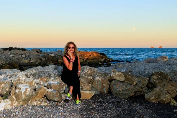 日落时坐在海滩岩石上的西班牙裔女性 — 图库照片