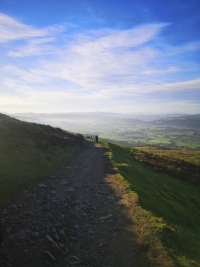 Wrexham 'da güneşli bir günde, uzaktan sisli manzaraya doğru yürüyen bir adamla bir tepe yolu.