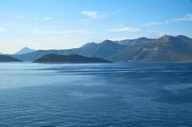 Huzurlu gökyüzünün altındaki sakin deniz dalgalarının yanındaki tepelerin manzarası