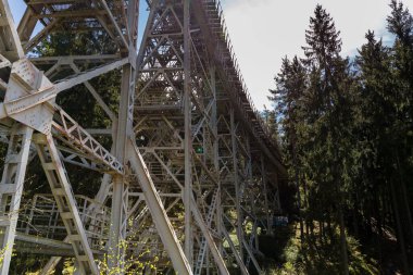 Yeşil ağaçlarla çevrili metalik bir yapının yakından çekimi, Ziemestal Köprüsü.
